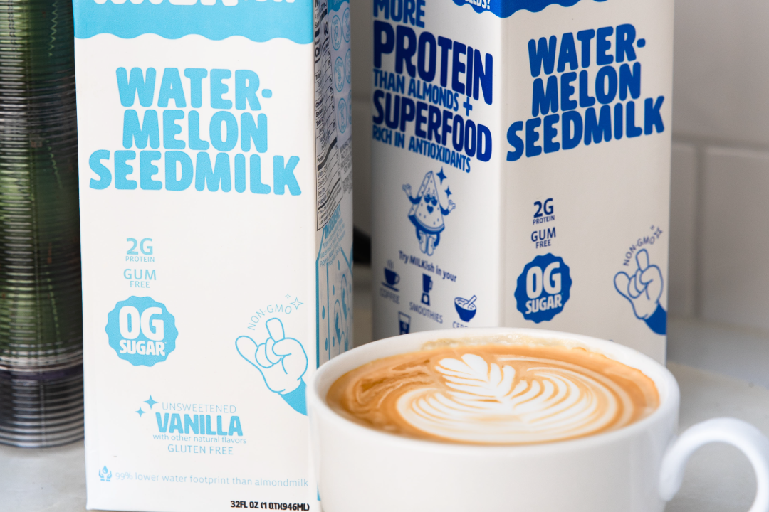 Two cartons of Milkish watermelon seedmilk with a cup of coffee on a surface.