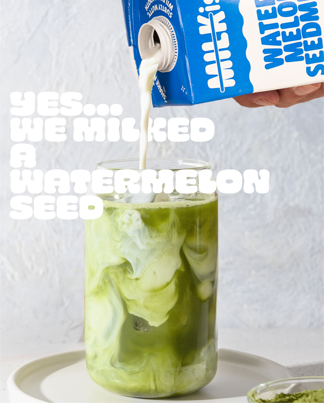 Person pouring milk from a carton into a glass with ice and matcha, text overlay 'YES... WE MILKED A WATERMELON SEED'.